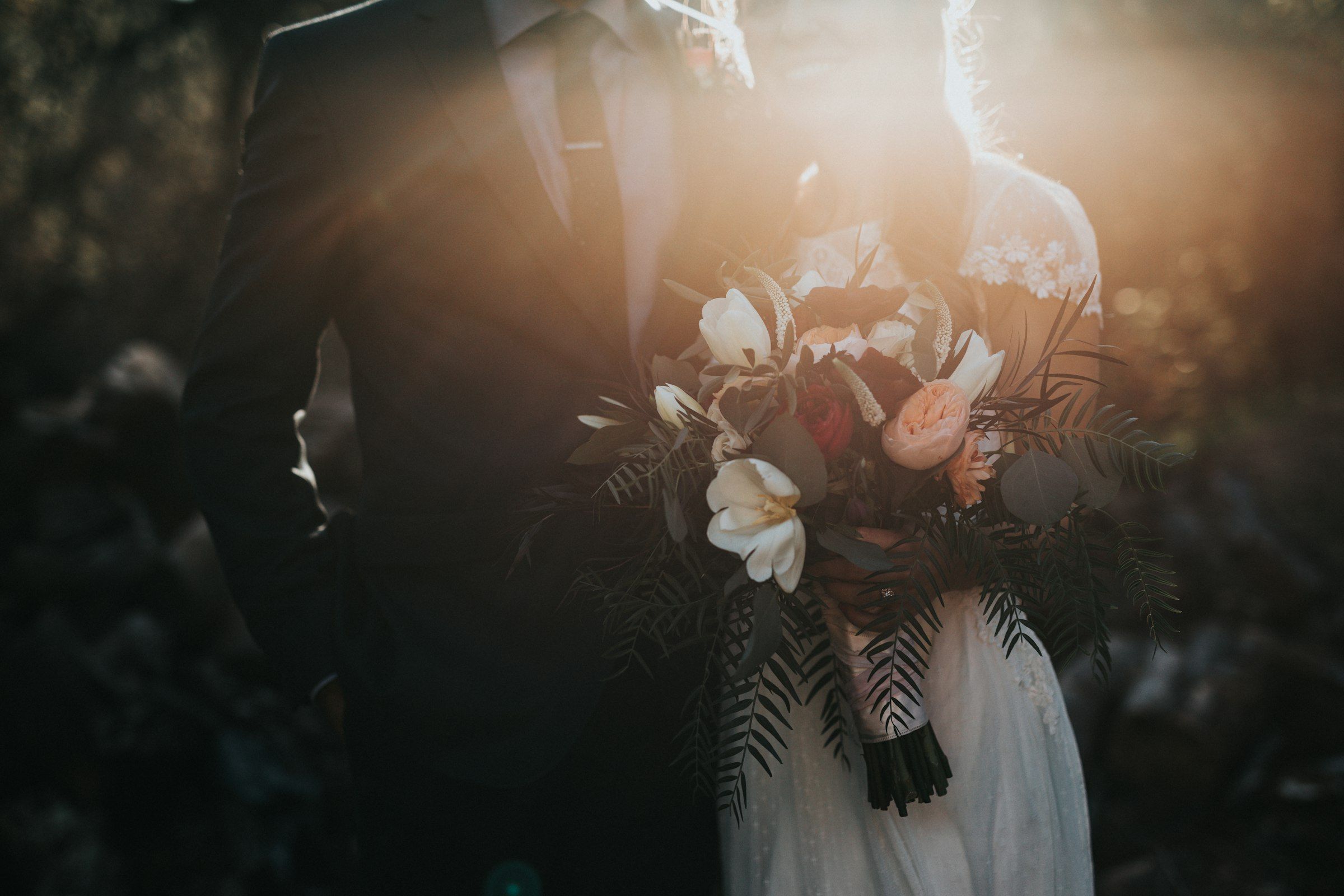 The couple embracing with the bouquet, backlit by the sunset