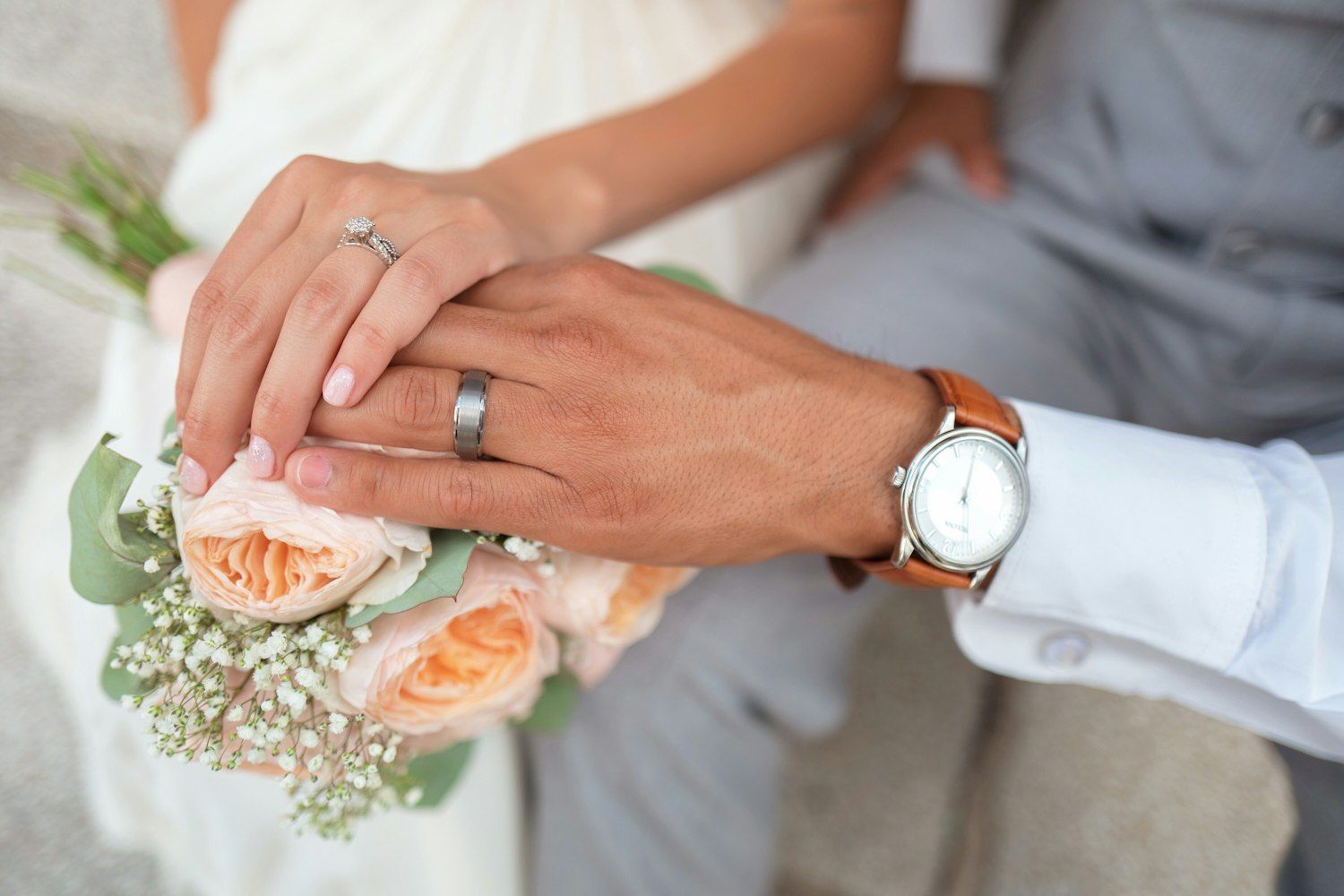 The couple's hands with wedding rings resting on a bouquet of roses